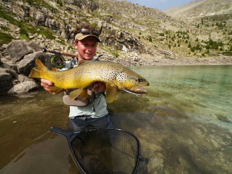 Un pêcheur souriant tient une grande truite brune lors d'un stage de pêche au Lac de Caillauas.