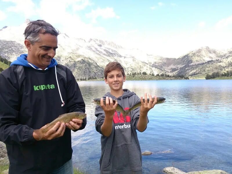 Un homme et un garçon souriants tiennent chacun une truite pêchée lors d'un stage de pêche au Lac de Caillauas.