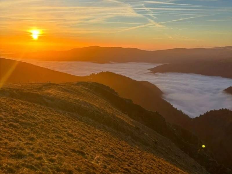 Coucher de soleil sur une vallée avec des collines et un ciel aux couleurs chaudes orangées et jaunes.