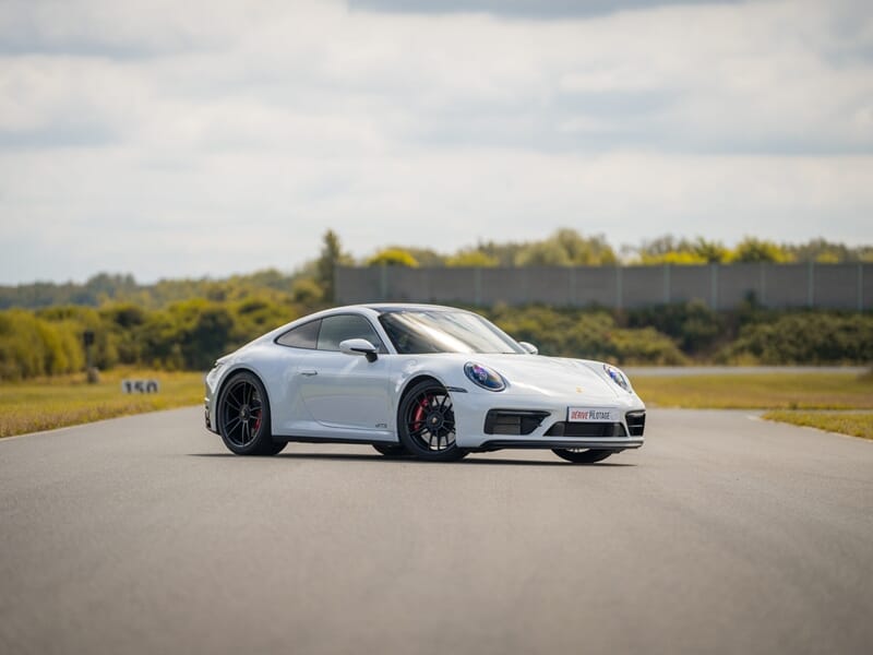 Voiture de sport blanche garée sur une piste de course avec un paysage verdoyant en arrière-plan, lors d'un coaching de pilotage sur circuit.