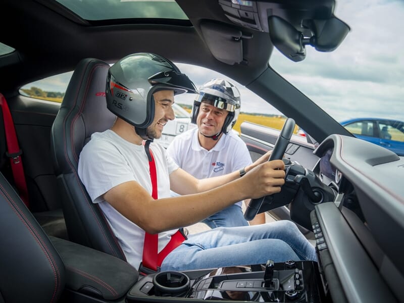 Deux hommes portant des casques de sécurité souriants à l'intérieur d'une voiture de sport lors d'un coaching de pilotage sur circuit.