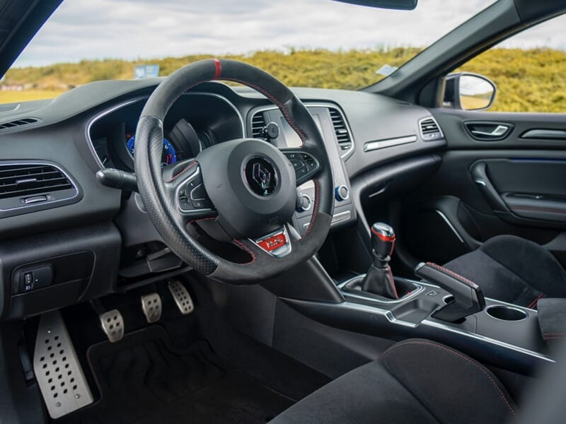 Intérieur d'une voiture sportive avec volant, levier de vitesse et sièges en cuir noir visibles, lors d'un coaching de pilotage sur circuit.