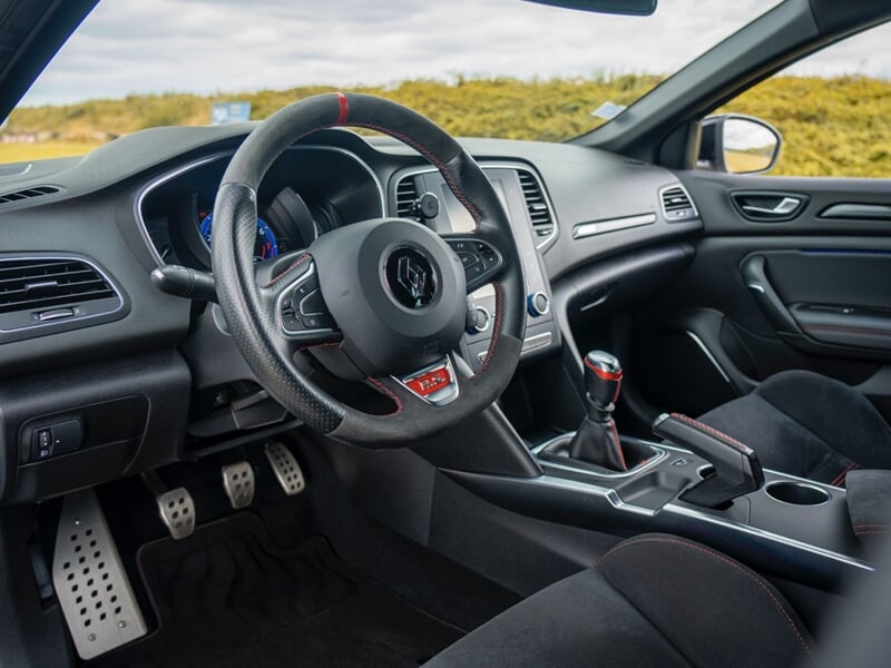 Intérieur d'une voiture sportive avec volant, levier de vitesse et sièges en cuir noir visibles, lors d'un coaching de pilotage sur circuit.