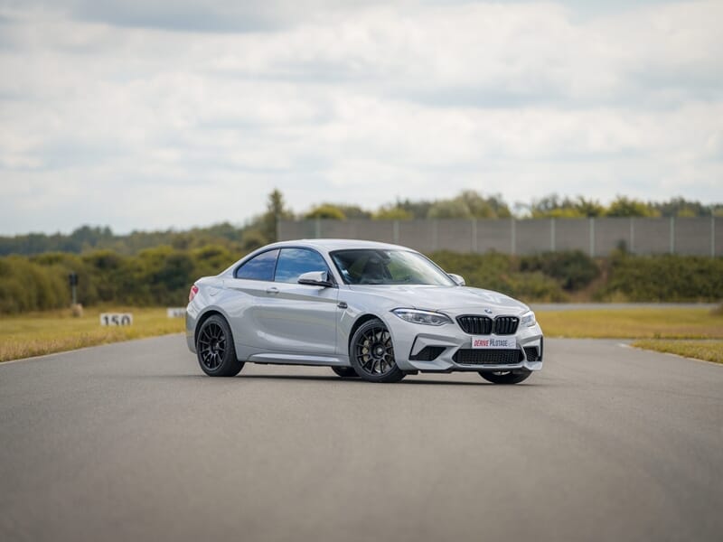 Voiture sportive blanche BMW M2 sur circuit de pilotage avec environnement naturel lors d'un coaching pilotage sur circuit.