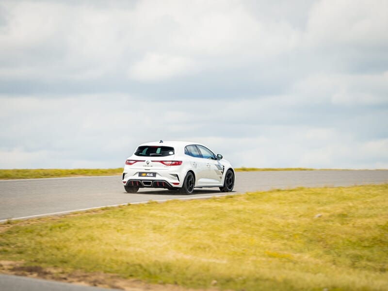 Voiture blanche sur circuit de course, virage à droite, ciel nuageux, lors d'un coaching pilotage sur circuit.