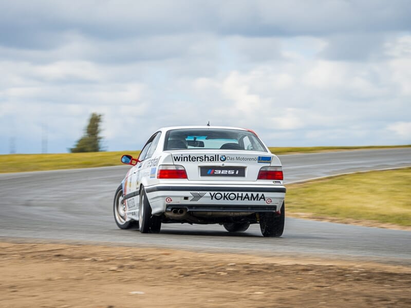 Vue arrière d'une voiture BMW de course blanche avec logos et sponsors lors d'un stage de pilotage glisse sur circuit.