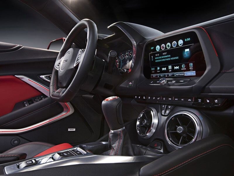 Intérieur moderne d'une voiture de sport avec volant, tableau de bord numérique et sièges en cuir rouge et noir.
