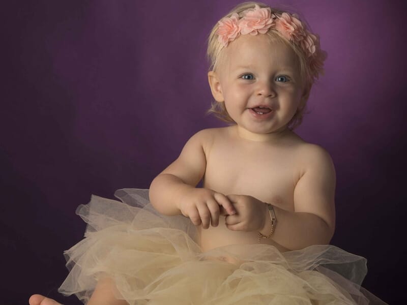 Jeune enfant souriante avec une jupe en tulle beige et un serre-tête fleuri lors d'un shooting bébé à Colmar.