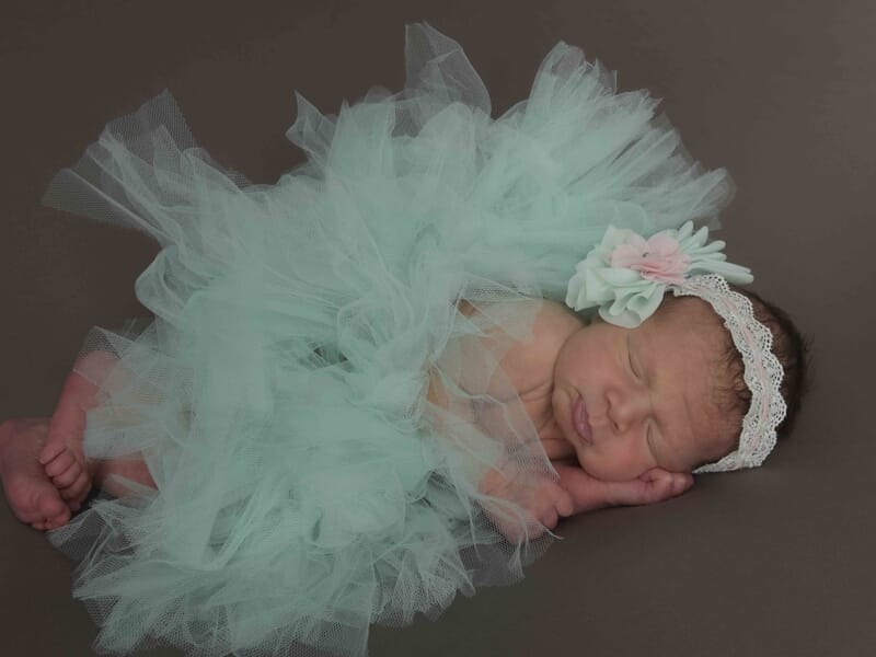 Nouveau-né endormi portant une robe verte en tulle et un bandeau fleuri, lors d'un shooting bébé à Colmar.