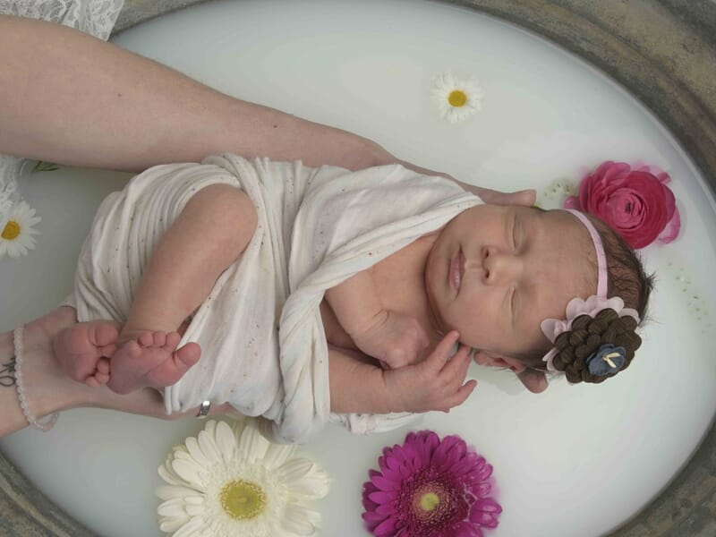 Bébé emmailloté dans un tissu blanc, flottant dans un bain de lait lors d'un shooting bébé à Colmar.