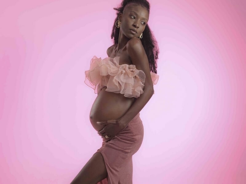 Femme enceinte en robe rose avec volants, posant de profil sur fond rose, lors d'un shooting photo grossesse à Colmar.