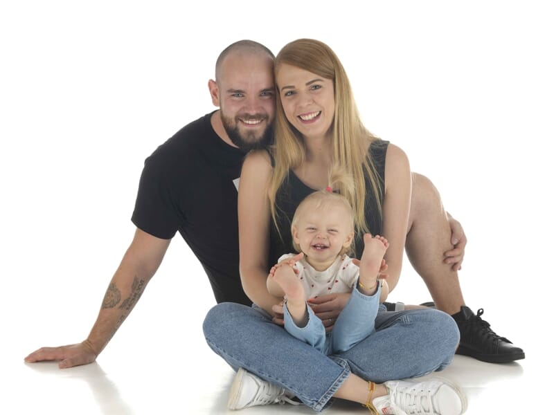 Un couple souriant assis au sol avec leur bébé joyeux entre eux, lors d'un shooting photo famille à Colmar.