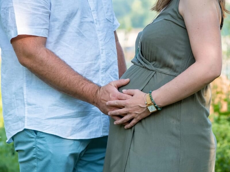 Un couple attend un bébé, l'homme et la femme enceinte se tiennent la main sur le ventre lors d'un shooting photo grossesse à Besançon.