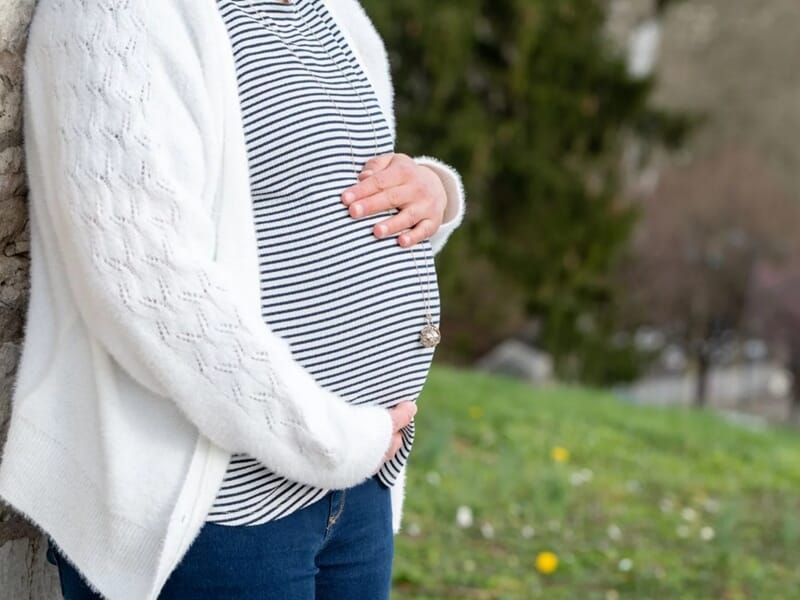 Femme enceinte en extérieur, portant un pull blanc et un t-shirt rayé, lors d'un shooting photo grossesse à Besançon.