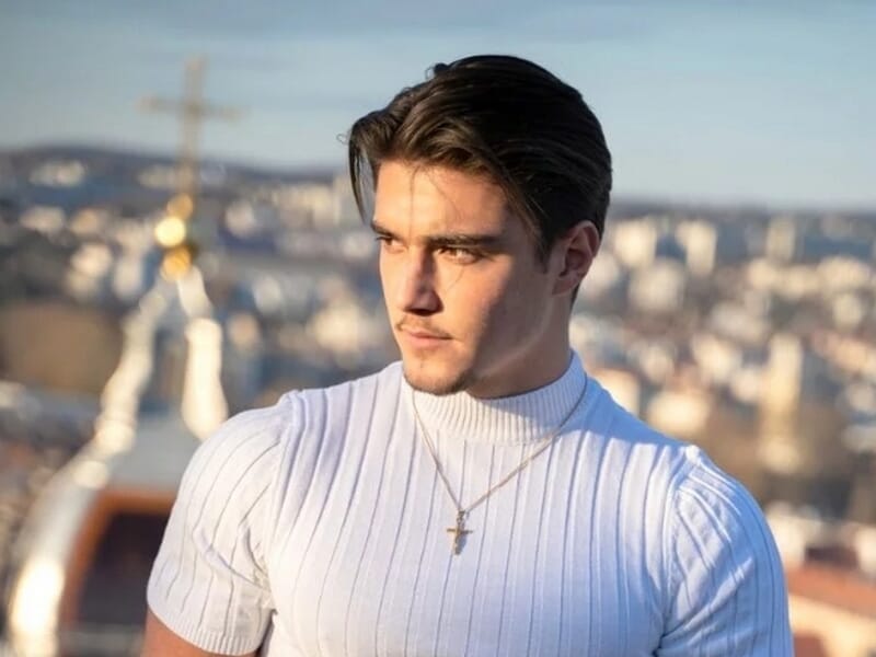 Jeune homme portant un pull blanc et un collier avec une croix, regardant vers la droite lors d'un shooting lifestyle à Besançon.