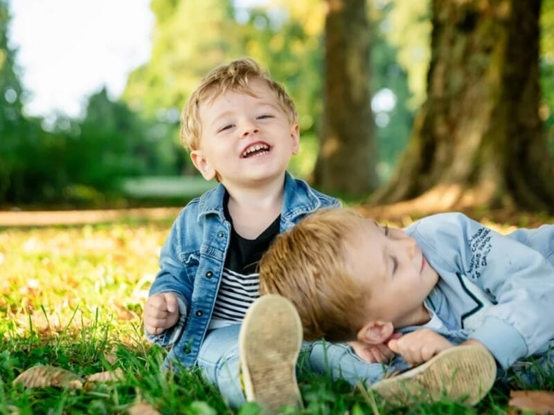 Deux jeunes garçons souriants allongés sur l'herbe verte dans un parc ensoleillé lors d'un shooting photo famille à Besançon.