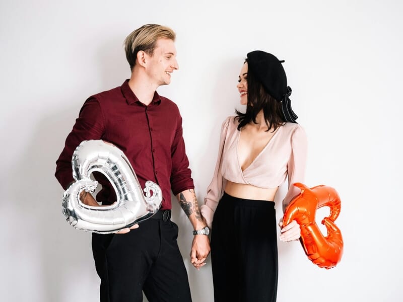 Un couple souriant se tenant la main, chacun tenant un ballon en forme de cœur lors d'un shooting photo couple à Besançon.