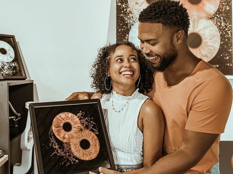 Couple souriant tenant un cadre avec une photo artistique d'iris d'yeux, ambiance chaleureuse et conviviale.