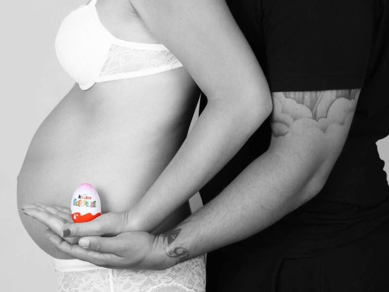Un couple en noir et blanc, la femme enceinte en sous-vêtements, tenant un œuf Kinder sur son ventre arrondi.