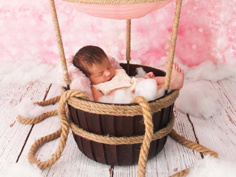 Nouveau-né dormant paisiblement dans un panier en bois suspendu, décoré avec une corde épaisse sur fond rose.