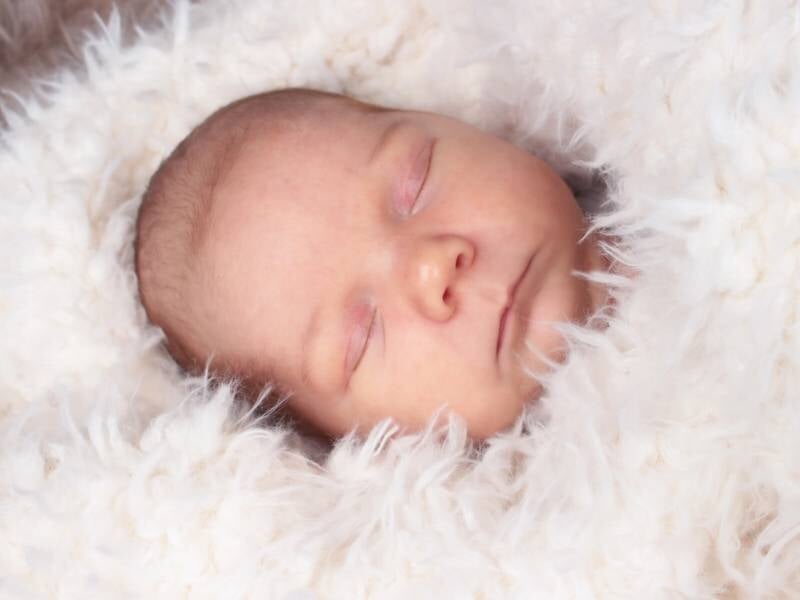 Portrait en gros plan d'un bébé endormi sur un tissu blanc duveteux, avec une expression calme et sereine.
