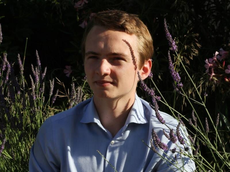 Jeune homme en chemise bleue assis dans un jardin avec de la lavande autour de lui, lors d'un shooting photo portrait.