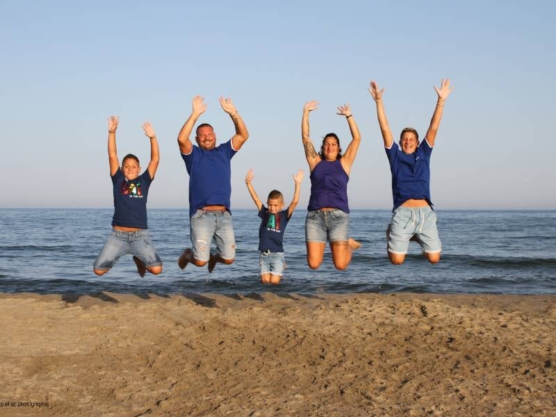 Une famille de cinq personnes saute joyeusement sur une plage au bord de la mer par une journée ensoleillée.