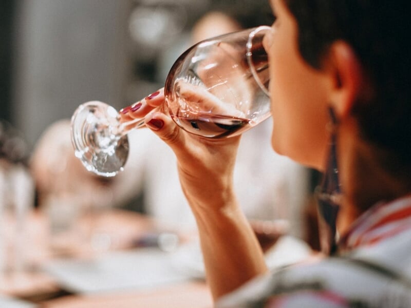 Personne dégustant un verre de vin rouge lors d'une séance d'oenologie en intérieur chaleureux.