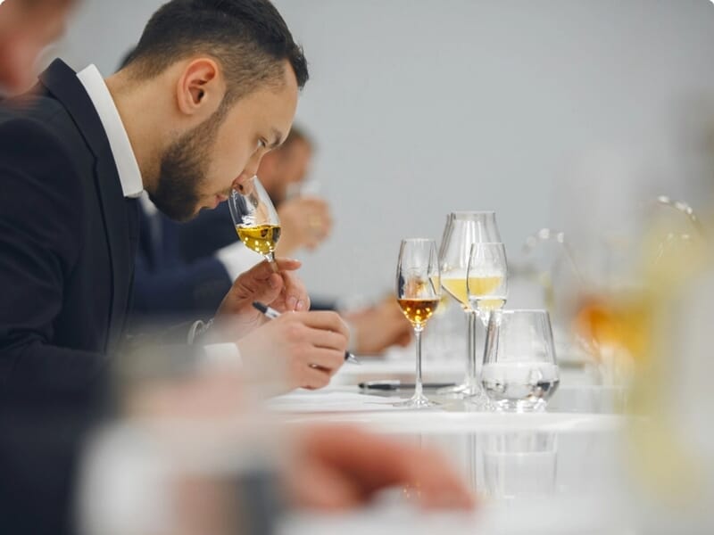 Homme concentré en train de sentir un verre de vin blanc lors d'une dégustation professionnelle.