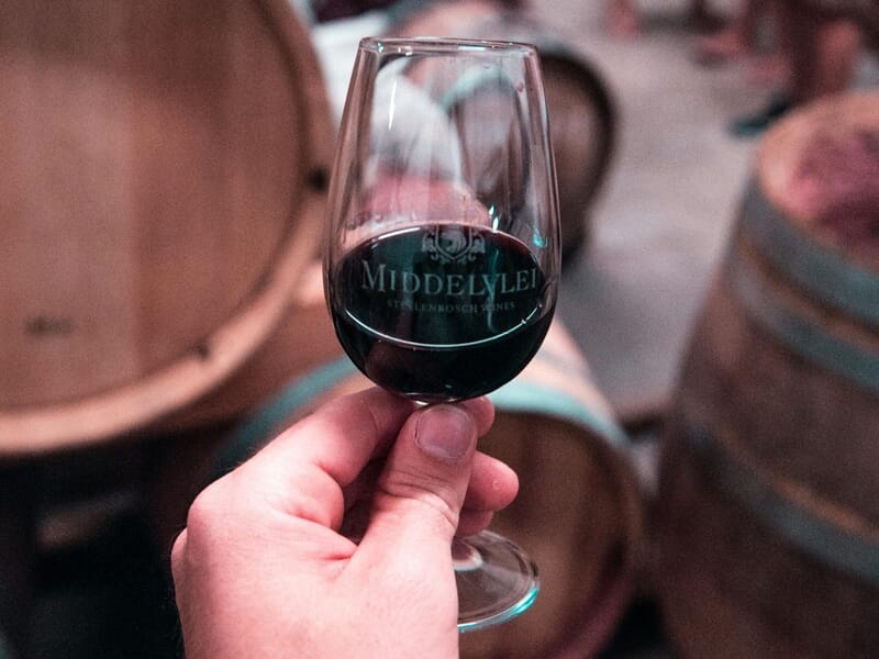 Main tenant un verre de vin rouge avec des tonneaux en arrière-plan dans une cave.