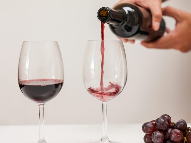 Vin rouge versé dans un verre à côté d'une grappe de raisin sur une table claire.