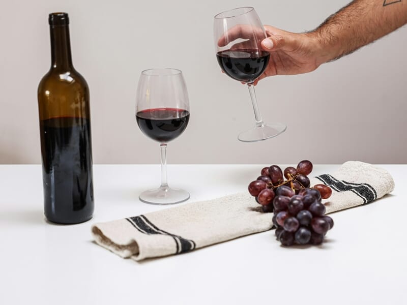 Verre de vin rouge posé sur une table avec une bouteille et des grappes de raisin.