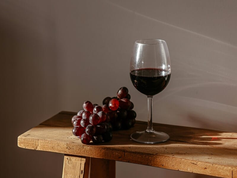 Verre de vin rouge rempli posé sur une table en bois à côté d'une grappe de raisin.