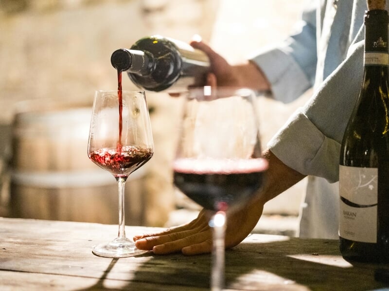 Un homme verse du vin rouge dans un verre à vin posé sur une table en bois dans une cave à vin rustique.