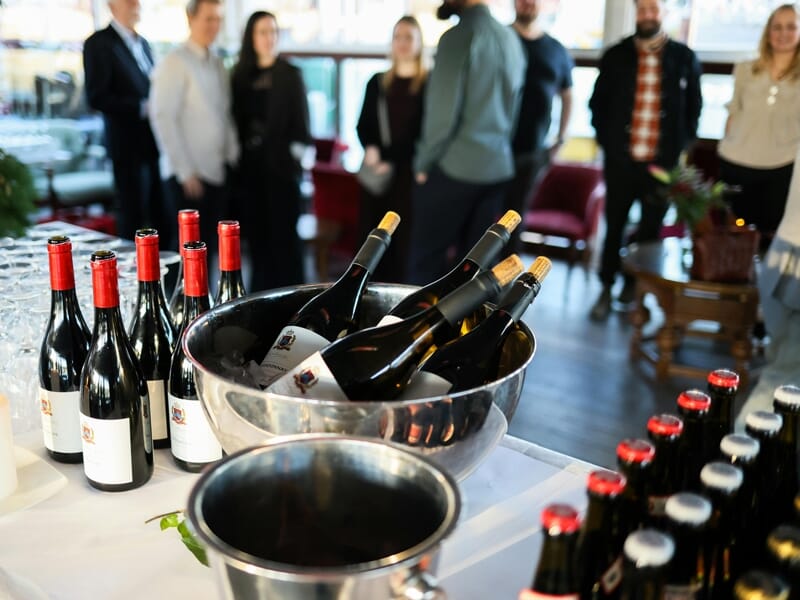 Bouteilles de vin rouge et blanc dans un seau à glace lors d'une dégustation avec plusieurs personnes en arrière-plan.