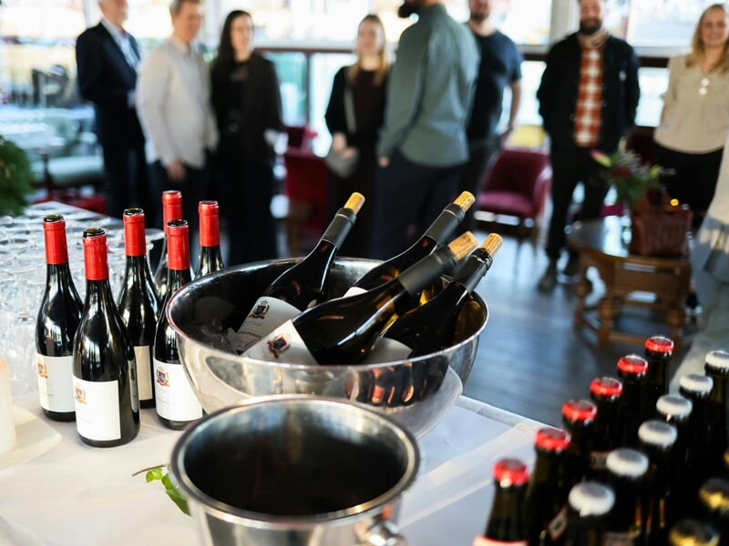 Bouteilles de vin rouge et blanc dans un seau à glace lors d'une dégustation avec plusieurs personnes en arrière-plan.