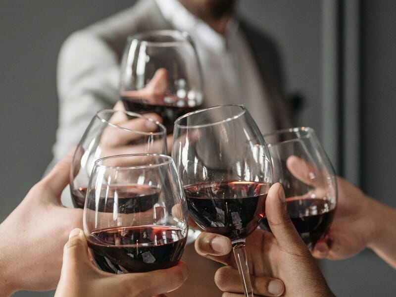 Quatre personnes trinquent avec des verres de vin rouge lors d'une réunion conviviale en intérieur.