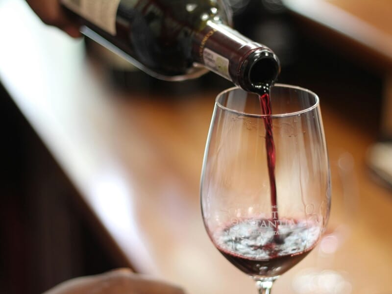 Un verre à vin est rempli de vin rouge versé depuis une bouteille, dans une ambiance chaleureuse et floue en arrière-plan.