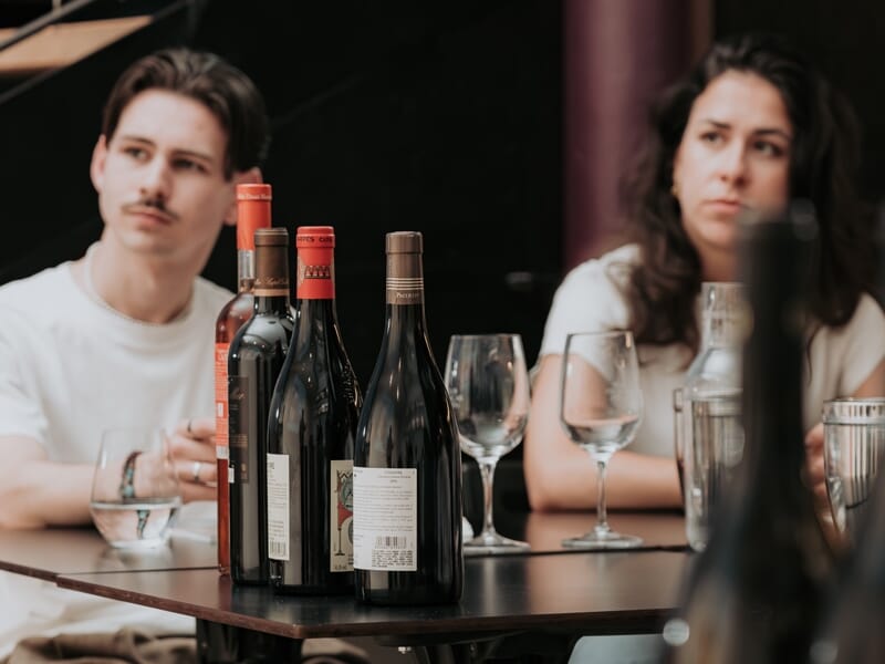 Deux personnes assises à une table avec plusieurs bouteilles de vin et des verres, en pleine dégustation œnologique.