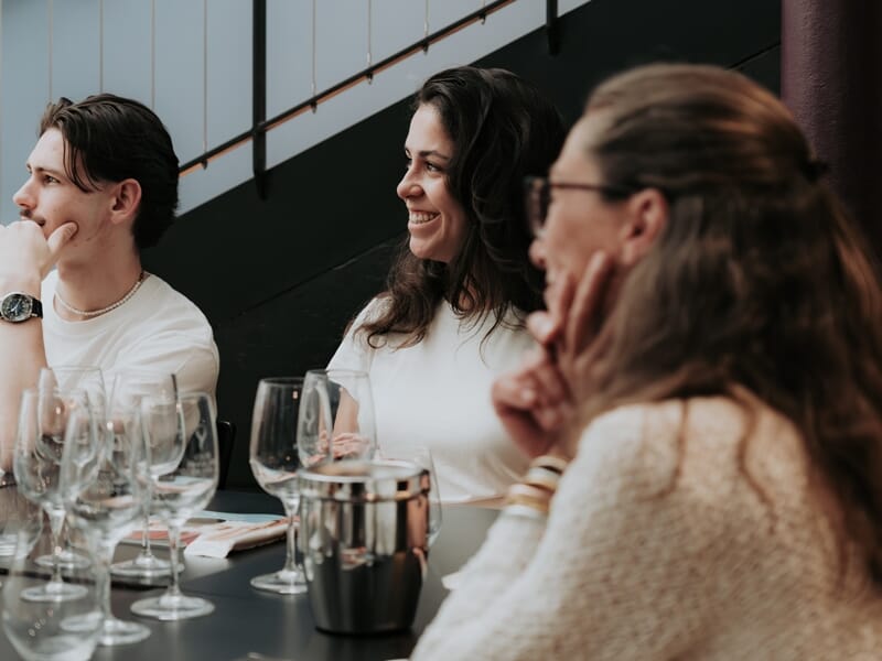 Trois personnes assises à une table avec plusieurs verres à vin, participant à une dégustation de vin en intérieur.