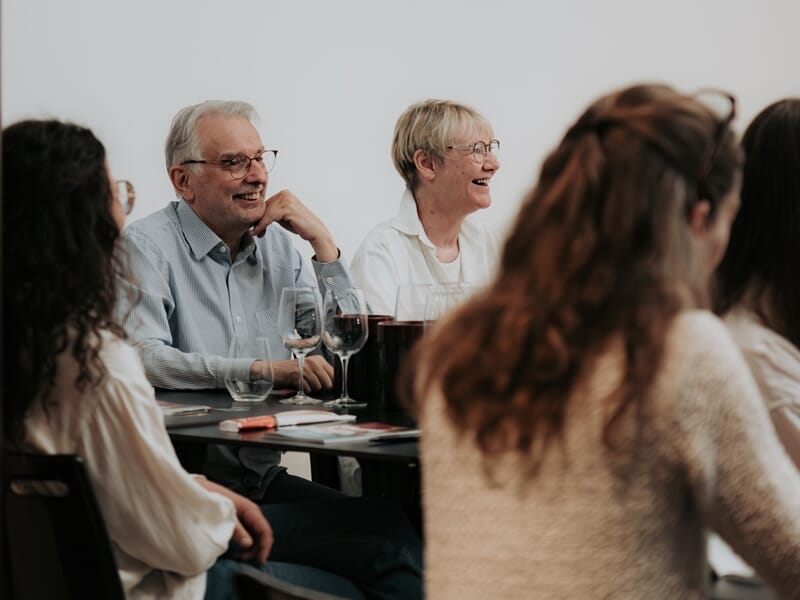 Groupe de personnes assises autour d'une table lors d'une dégustation de vin, avec verres et ambiance conviviale.