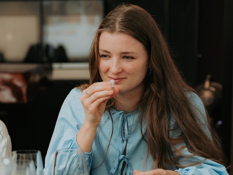 Jeune femme aux cheveux longs sentant un petit verre lors d'une dégustation de vin en intérieur chaleureux.