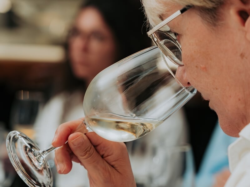 Personne âgée portant des lunettes sentant un verre de vin blanc lors d'une dégustation œnologique en Champagne.