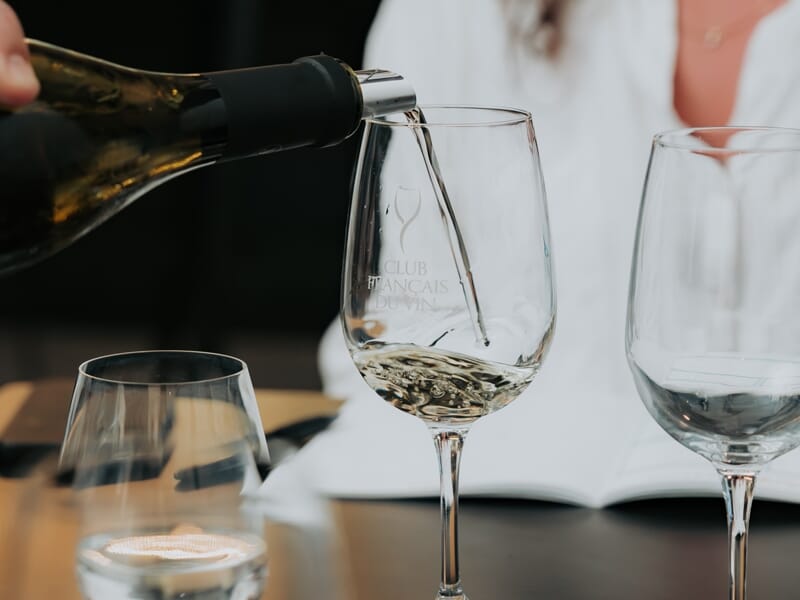 Un verre à vin blanc est rempli à partir d'une bouteille lors d'une dégustation dans un cadre élégant et convivial.