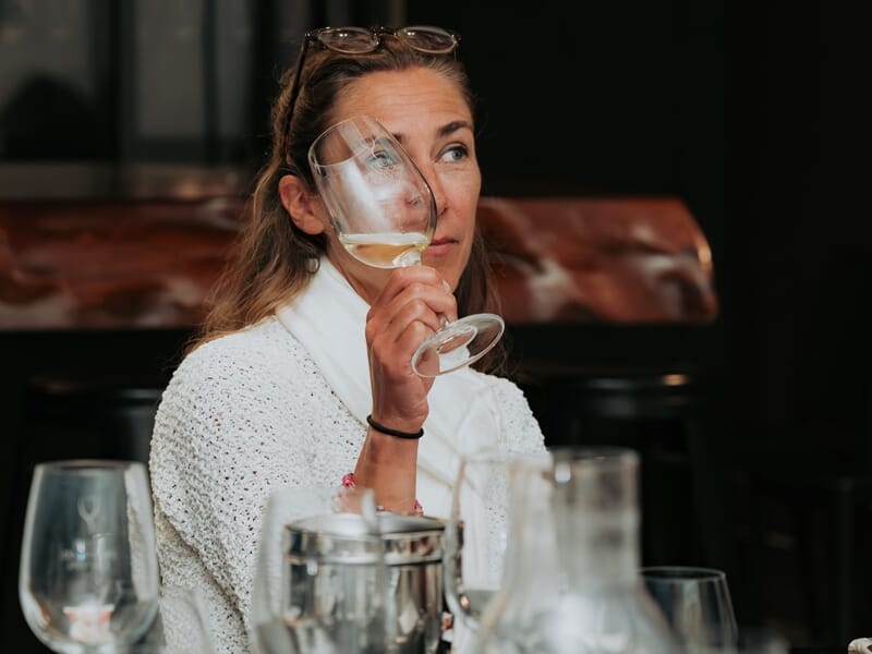 Femme dégustant un verre de vin blanc lors d'une séance d'oenologie dans une ambiance chaleureuse et conviviale.