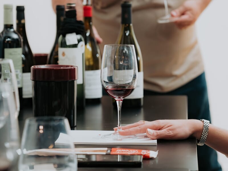 Dégustation de vin rouge avec plusieurs bouteilles en arrière-plan et une main posée sur la table noire.