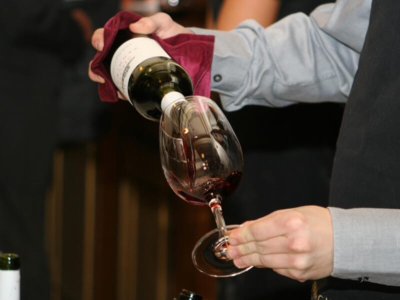 Un sommelier verse du vin rouge dans un verre à vin lors d'une dégustation dans un cadre élégant.