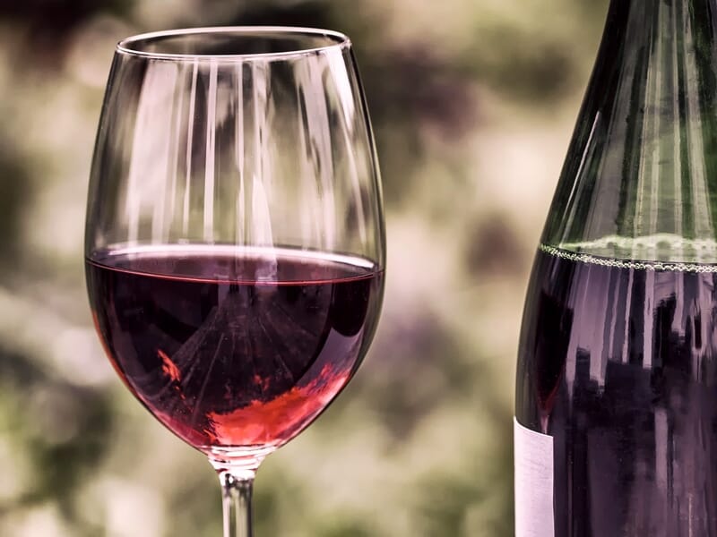 Verre de vin rouge rempli à moitié à côté d'une bouteille de vin avec une étiquette blanche floue en arrière-plan.