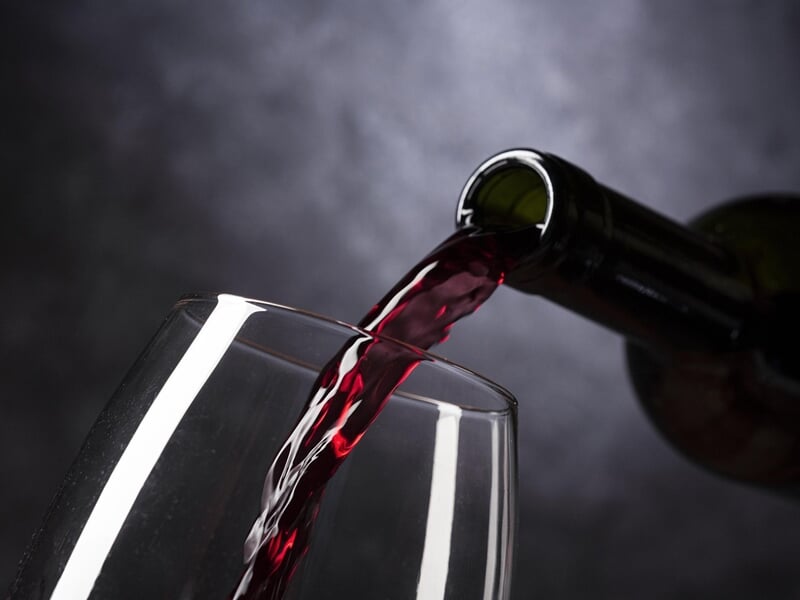 Vin rouge versé dans un verre à vin transparent, bouteille inclinée, fond sombre et flou, ambiance élégante et raffinée.