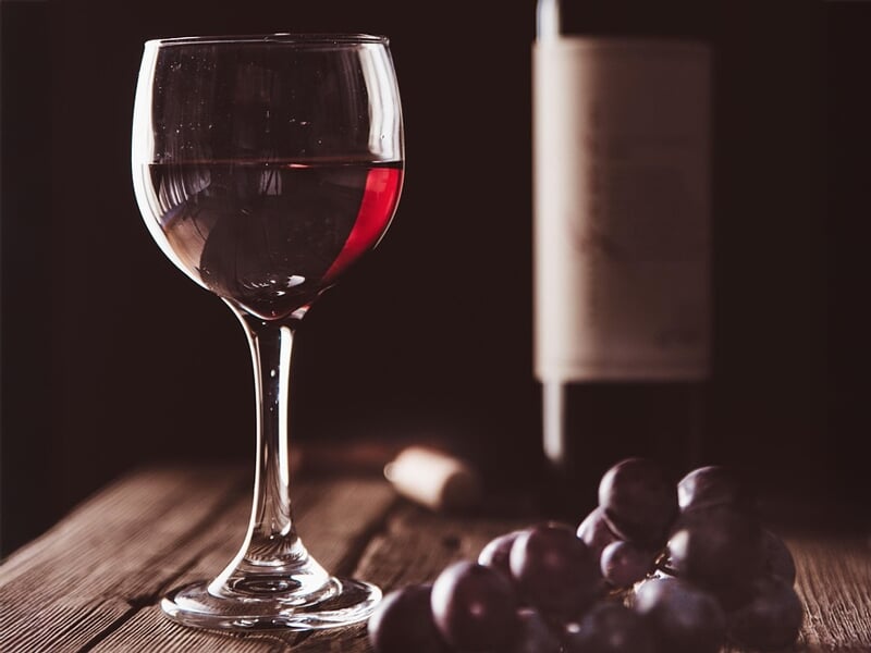Verre de vin rouge posé sur une table en bois avec une bouteille floue et des raisins au premier plan
